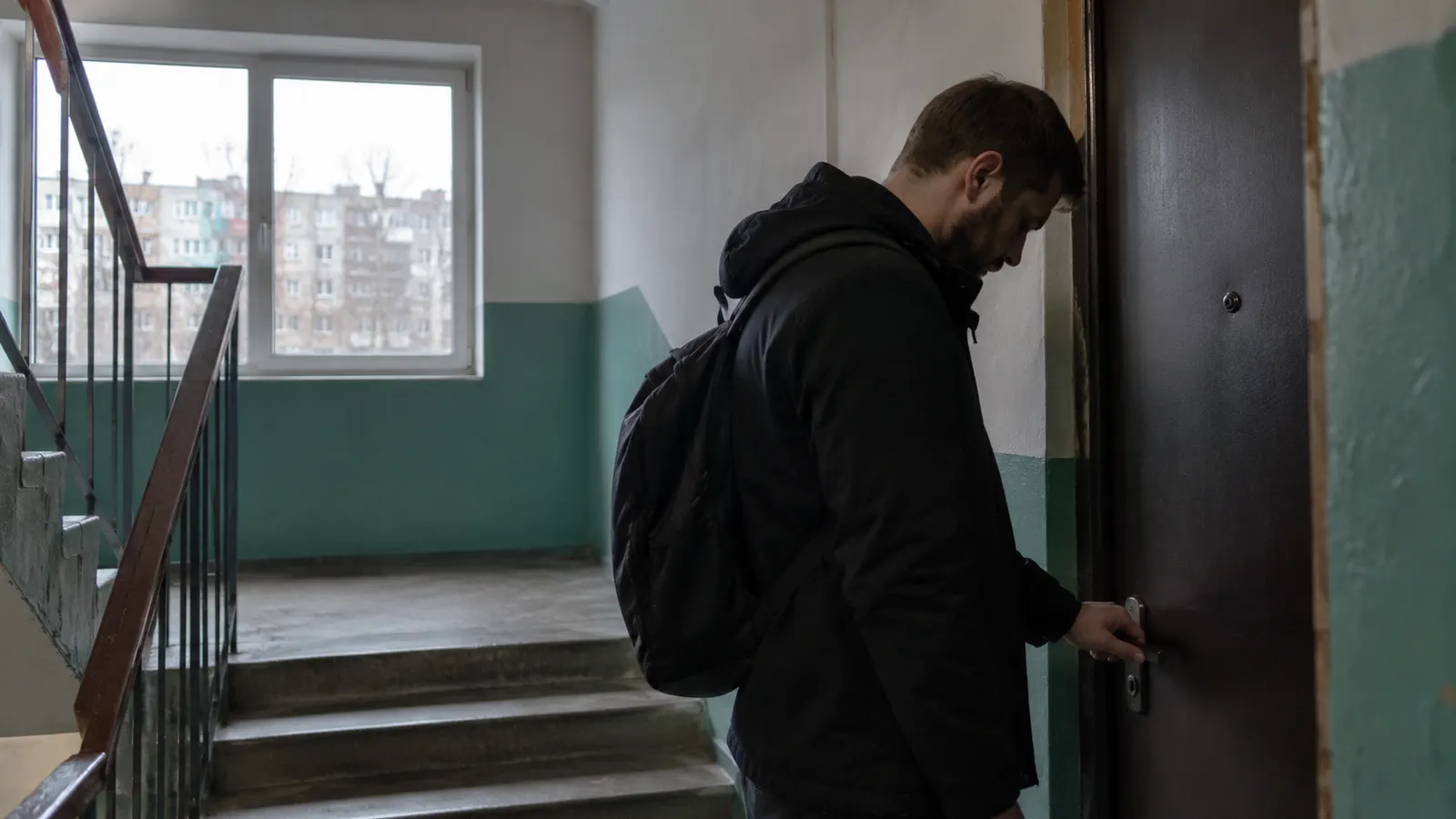 Чоловік з наплічником біля зачинених дверей у під’їзді — емоційний шантаж у стосунках
